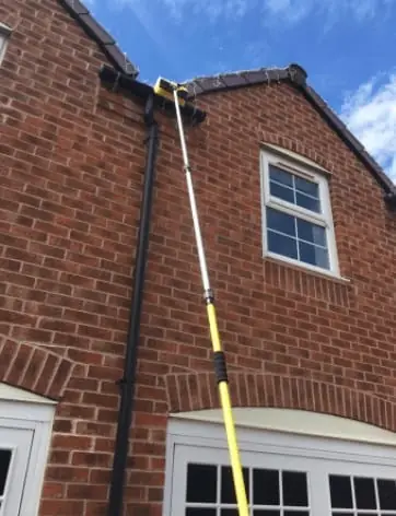 Gutter Vac Cleaning: Long yellow and white pole reaching up to the gutter of a two-storey brick house