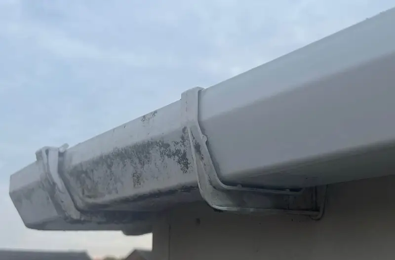Gutter Cleaning: Close view of a gutter joint and bracket with moss on one length and a clean length beside it